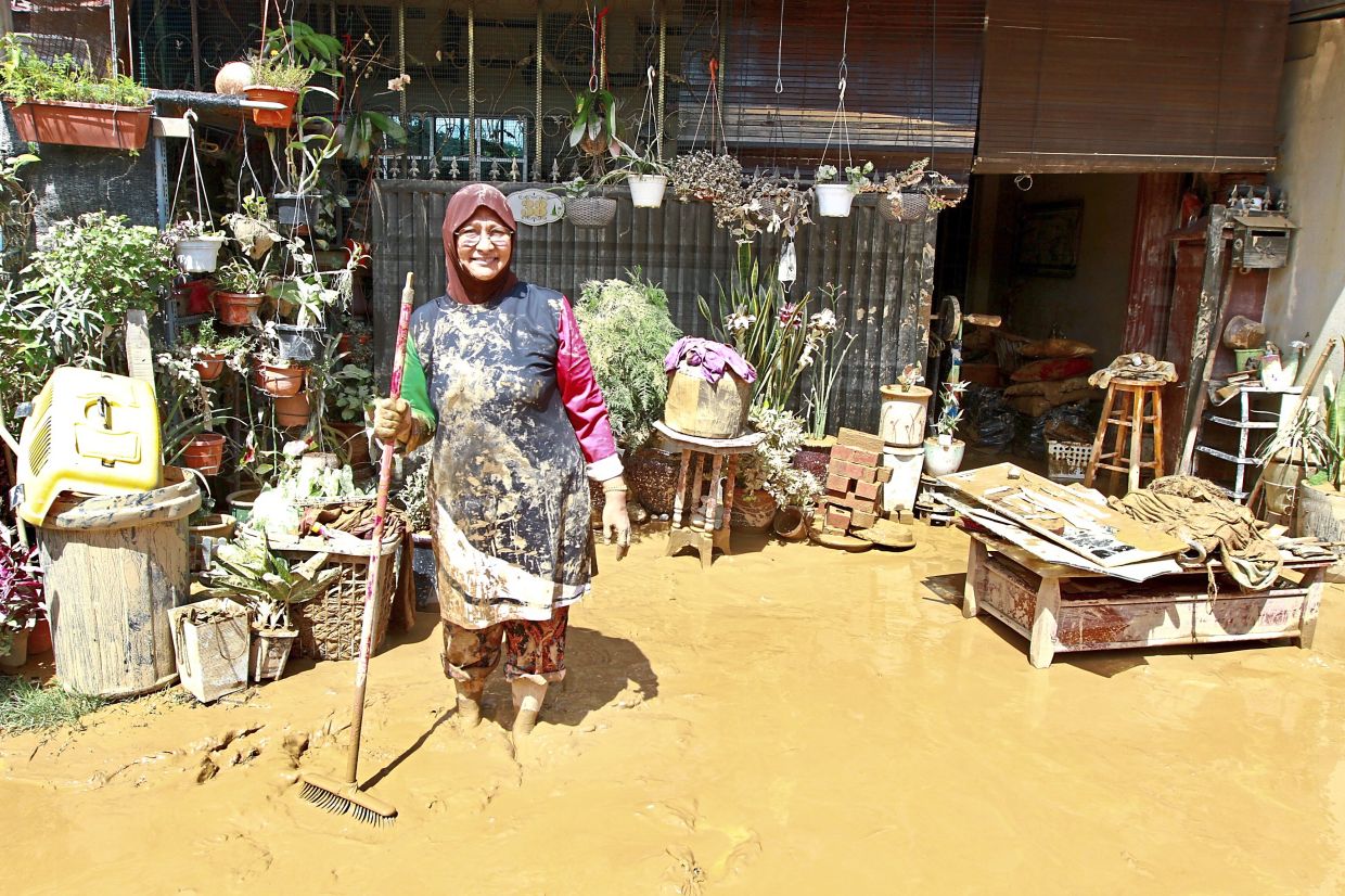A home owner manages to smile and maintain a positive attitude despite having to clean up the mud that has dirtied her home during the floods.