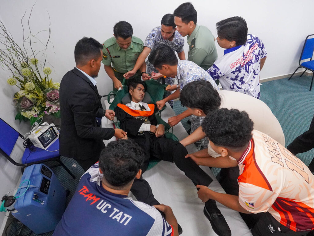 Coursemates, UC TATI staff and 96 HAT medical personnel help Muhammad Afiq on arrival for the convocation