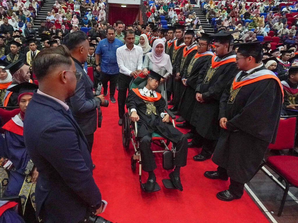 Fellow UC TATI graduates line the red carpet as Muhammad Afiq is wheeled to the convocation stage with his parents