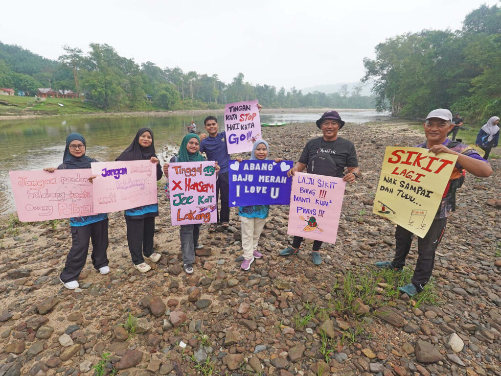 Hulu Berang residents holding handmade signs to cheer on kayakers by Sungai Berang