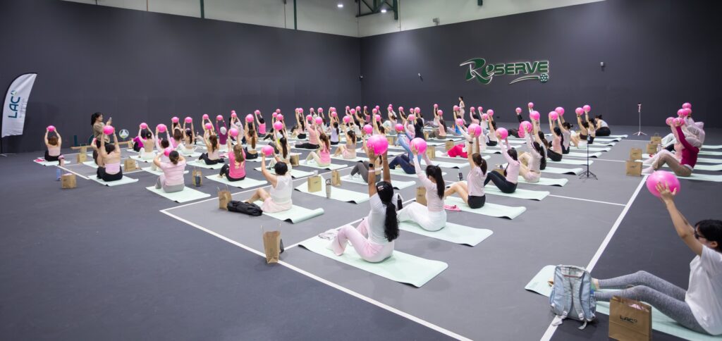 Women holding pink Pilates balls overhead during the LAC Community Pink-Lates Pilates session