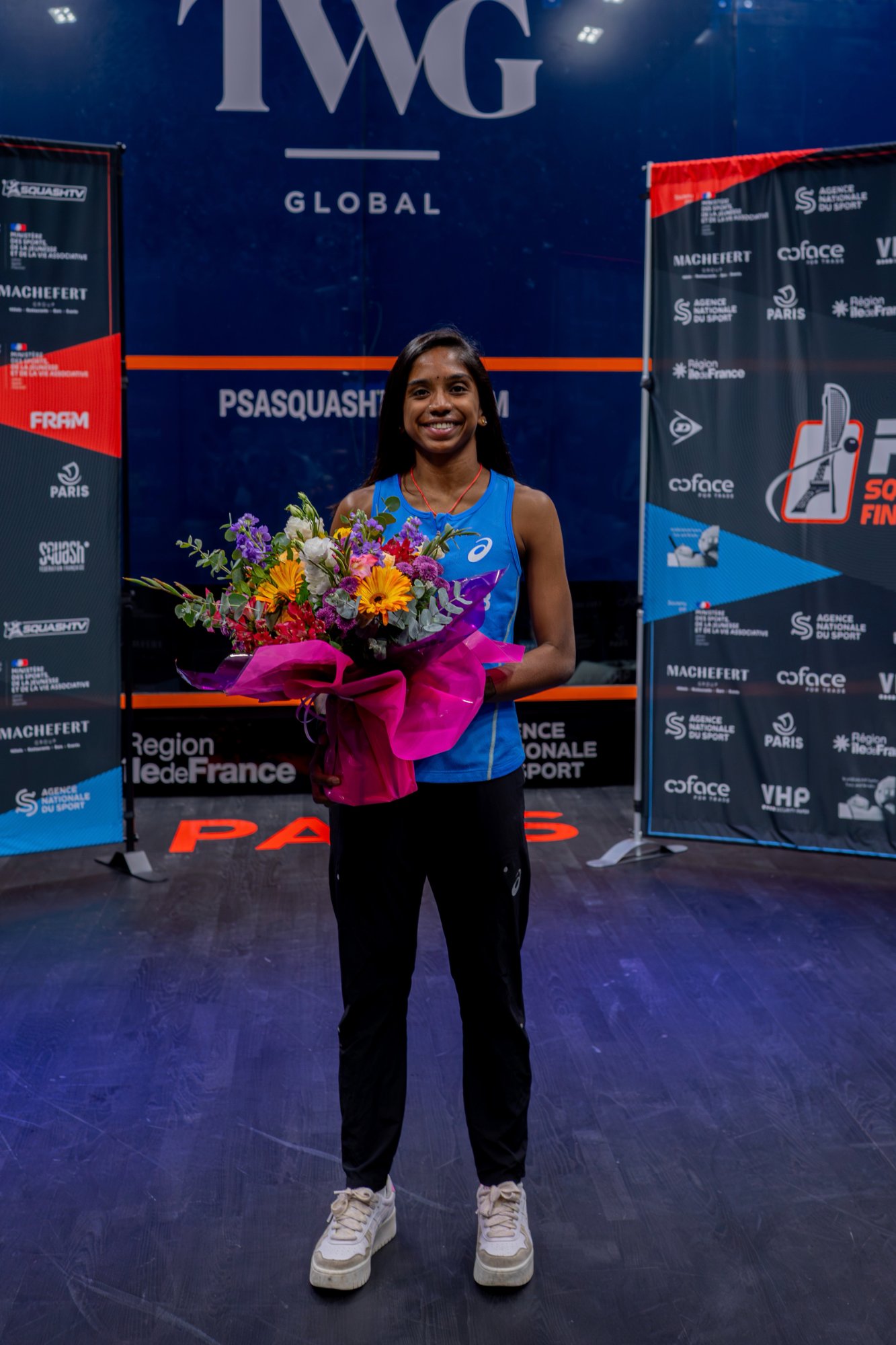 Sivasangari Subramaniam holding a bouquet of flowers on a glass squash court in Paris