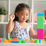 Young girl stacking colourful toy blocks, a simple play activity that supports toddler brain development