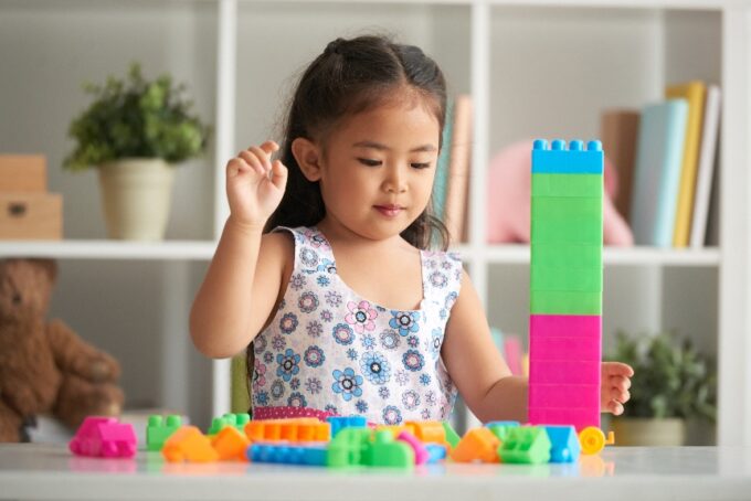 Young girl stacking colourful toy blocks, a simple play activity that supports toddler brain development